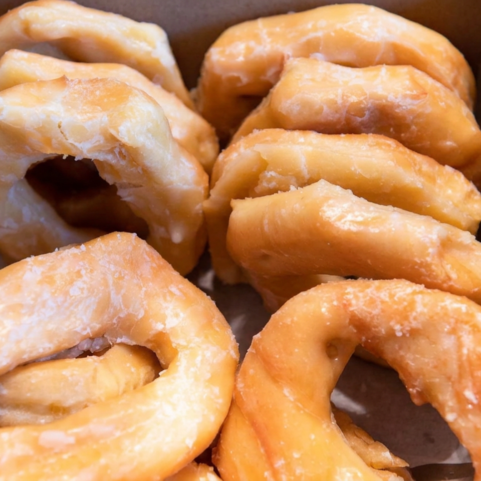 Box filled with assorted golden glazed doughnuts, including ring-shaped and twisted pastries.